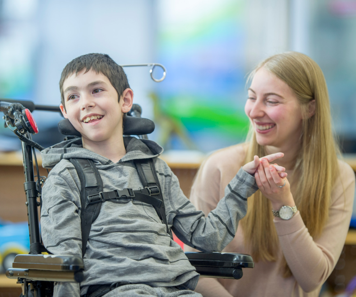 A woman holding the hand of a child in a wheelchair