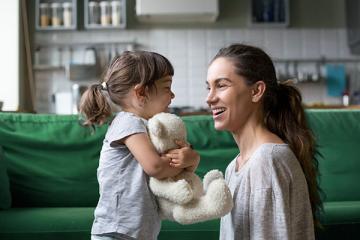 A child holding a teddy bear and a woman, each smiling at the other